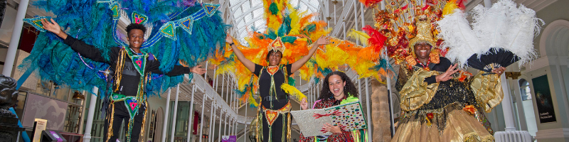 Four young people in Caribbean carnival costumes, smiling.