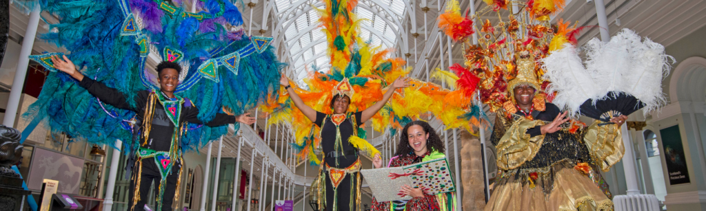 Four young people in brightly coloured Caribbean carnival costumes, smiling.