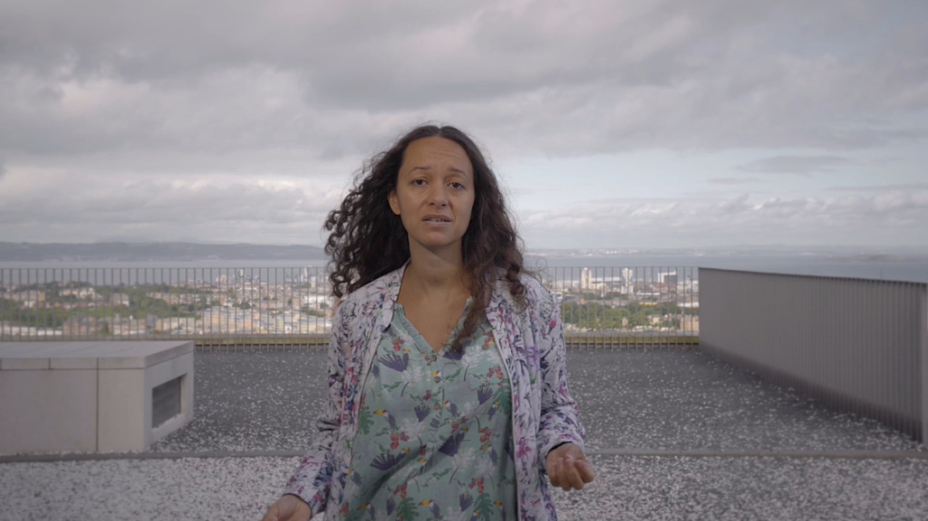 woman gesturing, curly hair blowing in wind, cityscape behind her