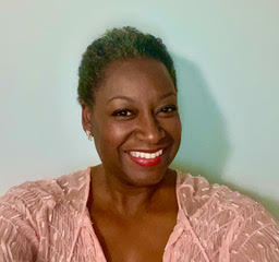 Black woman smiles at the camera, wearing a pink top