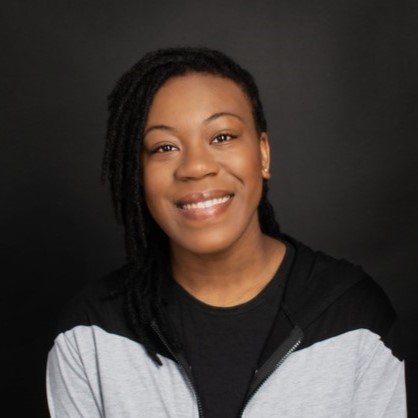 Person with brown skin wearing a white and black sweatshirt smiles at camera.